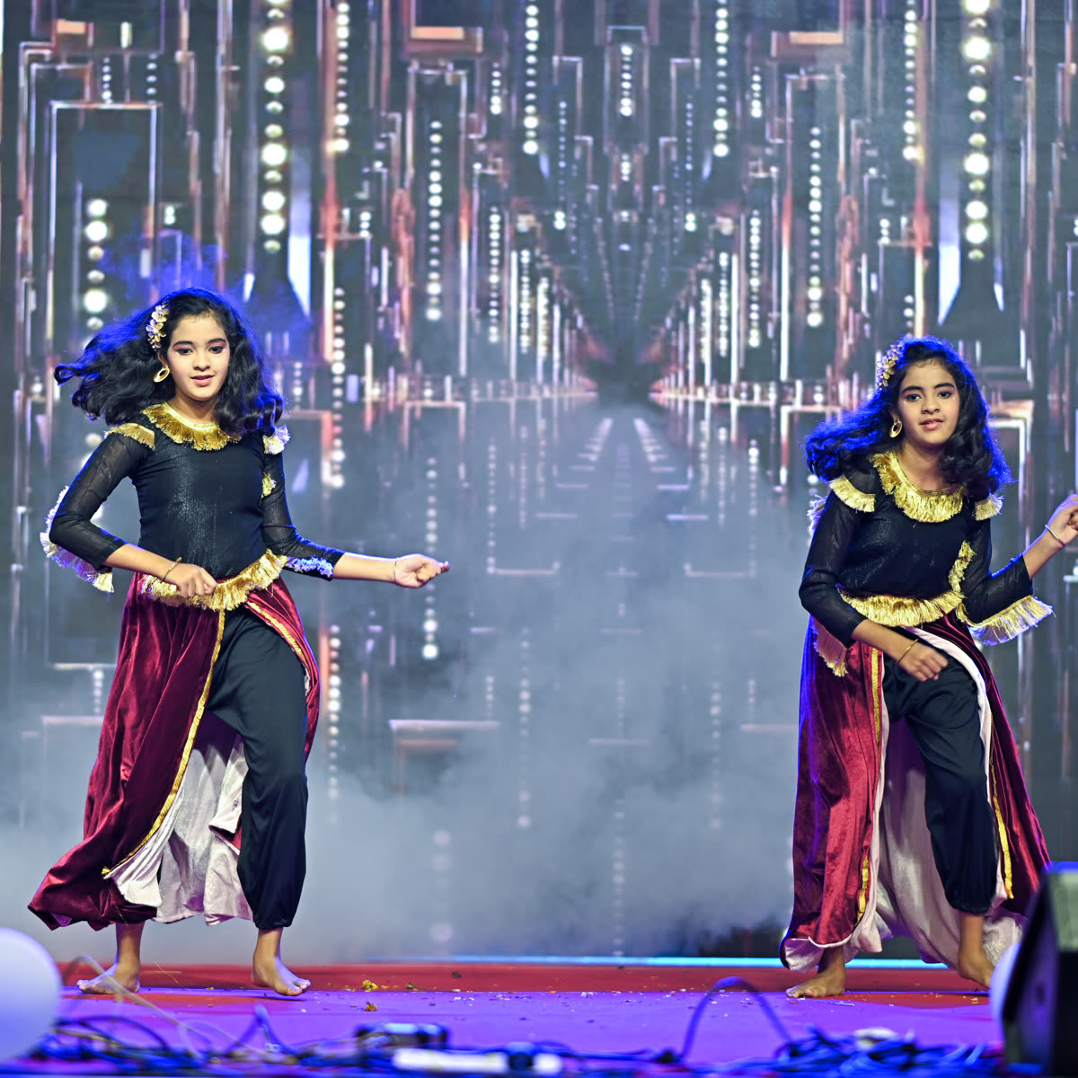 Two dancers in deep blue and gold costumes performing together on a smoke-lit stage