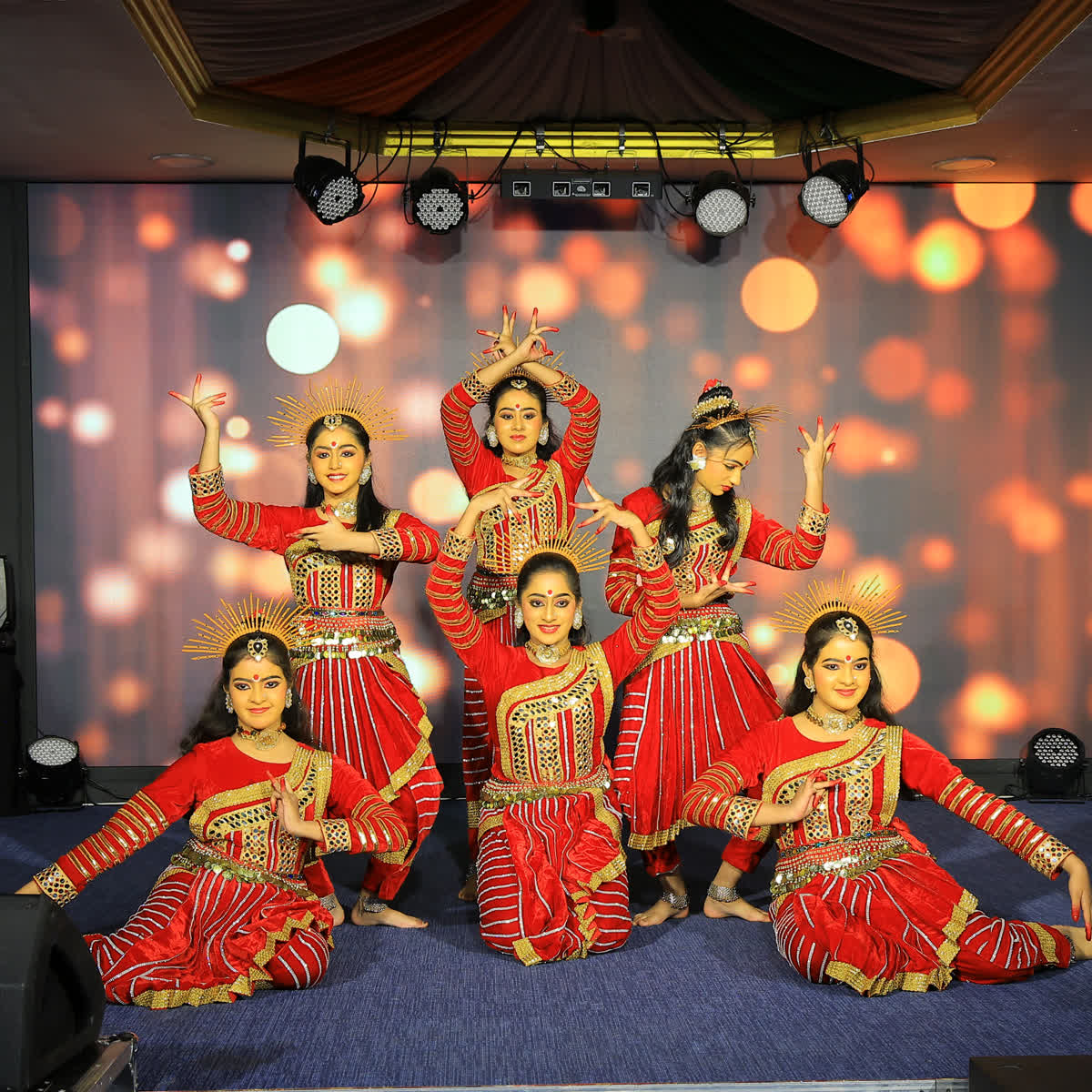 Young girls in red and gold costumes performing a classical dance on stage
