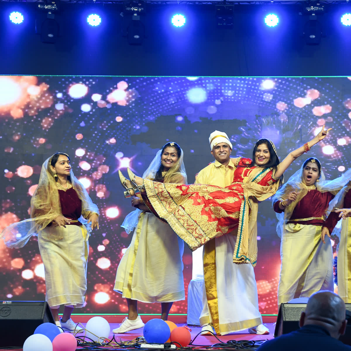 Dancers in cream and gold kasavu performing together under blue stage lighting
