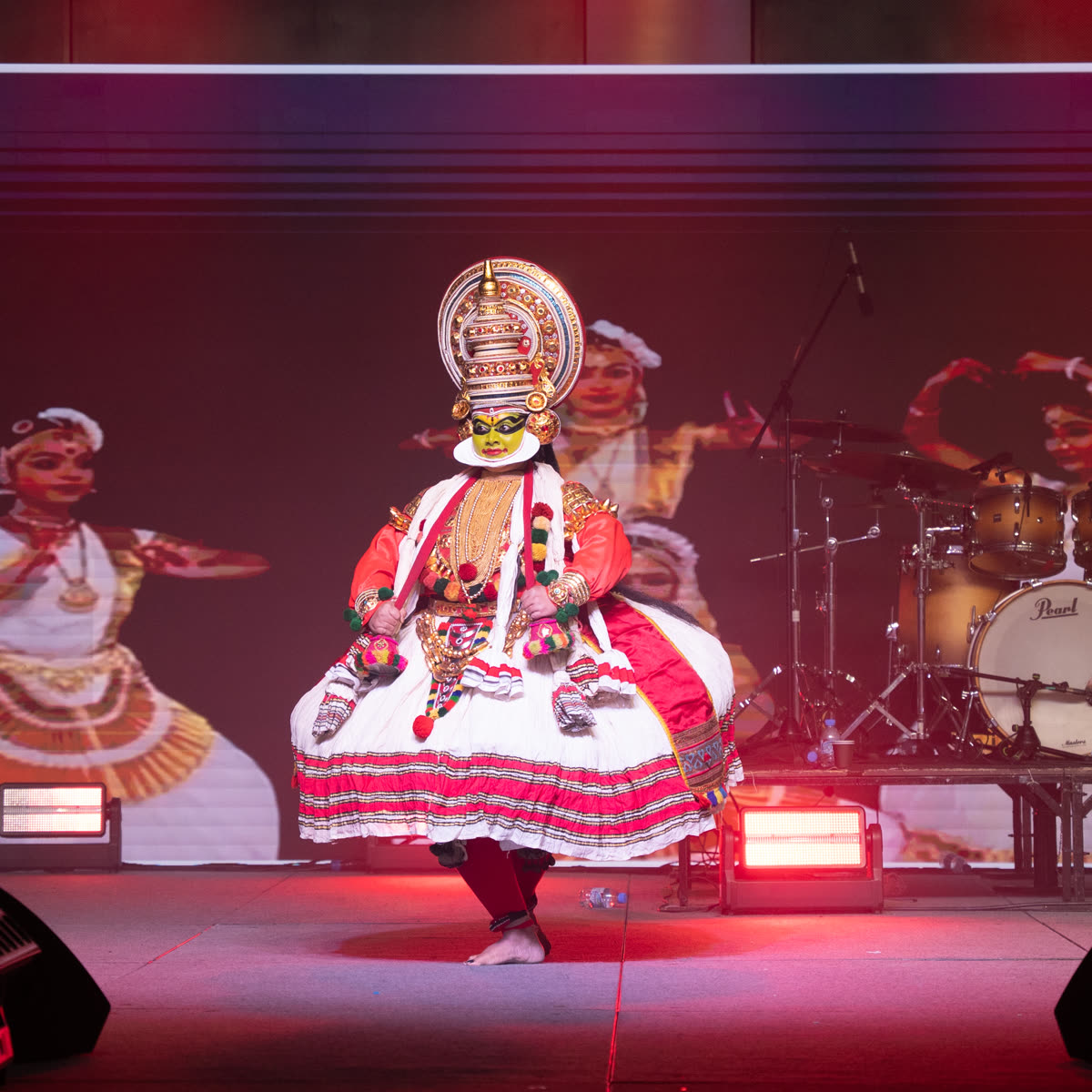 A Kathakali artist in full green face paint, crown and layered costume performing on stage
