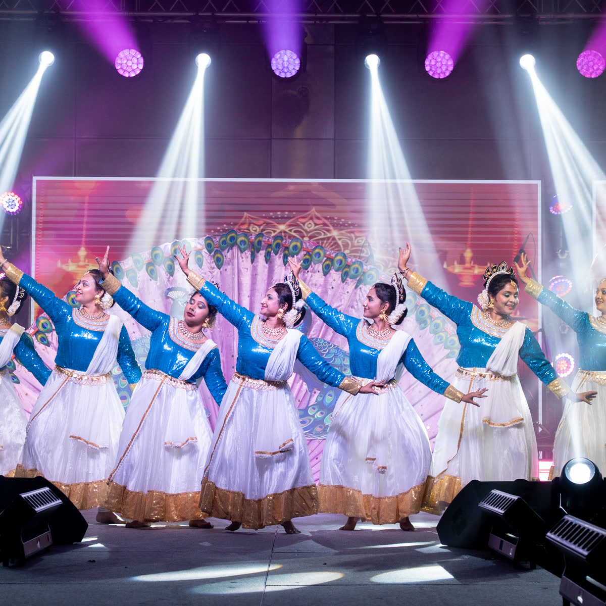 A large troupe in blue and white costumes performing a synchronised dance on stage
