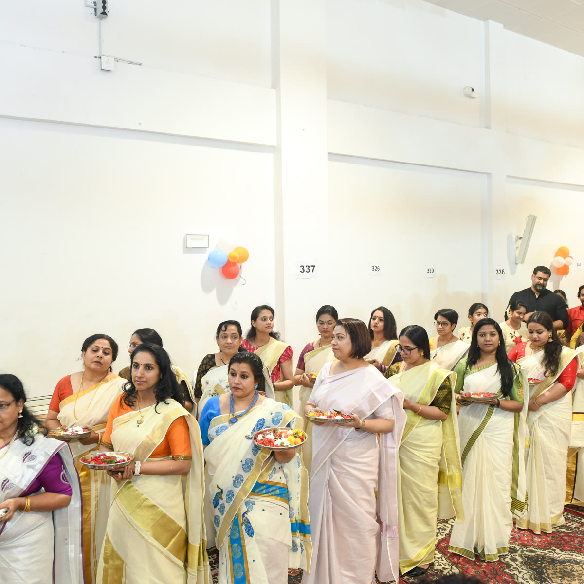 Women in kasavu sarees gathered in a hall before the Onam celebrations begin