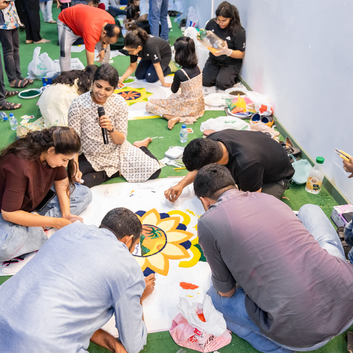 Members kneeling together to lay out a circular pookalam from coloured flower petals