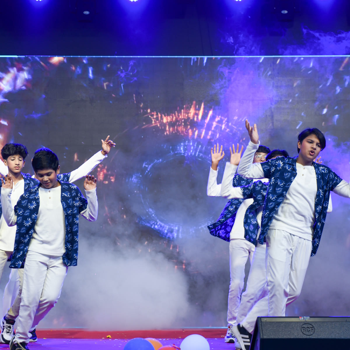 Young members performing an energetic group dance under blue stage lights